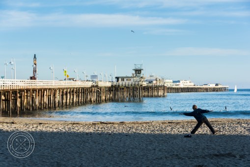 A man doing Yoga in the morning at the Santa Cruz Beach, with the pier in front of him, California, USA.